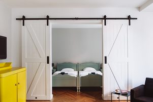 styl modern retro, apartamenty do wynajęcia Wrocław, drzwi przesuwne dwuskrzydłowe, drzwi przesuwne podwójne, drzwi przesuwne białe, drzwi przesuwne barn door, żółta komoda w salonie, podwójne drzwi do sypialni, podwójne łóżko w sypialni