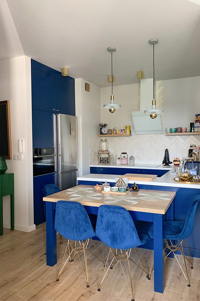 kuchnia w stylu nowoczesnym, niebieskie meble do kuchni, złote dodatki w kuchni, niebieskie krzesła w jadalni, lampy wiszące do kuchni