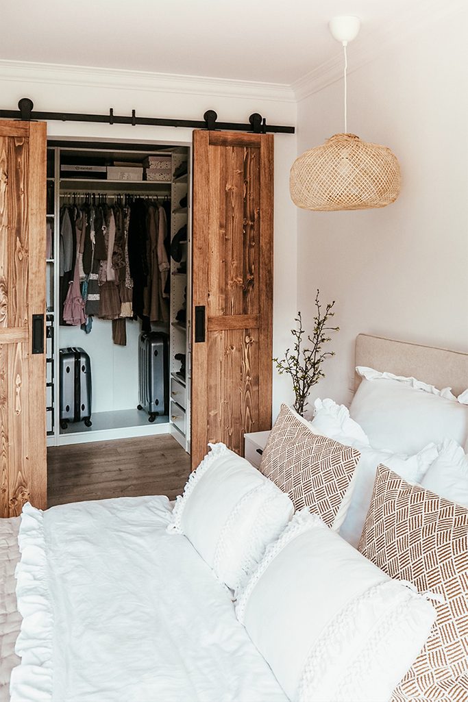 garderoba w sypialni, rozsuwane drzwi przesuwne, drewno i biel, ozdobne poduszki na łóżko