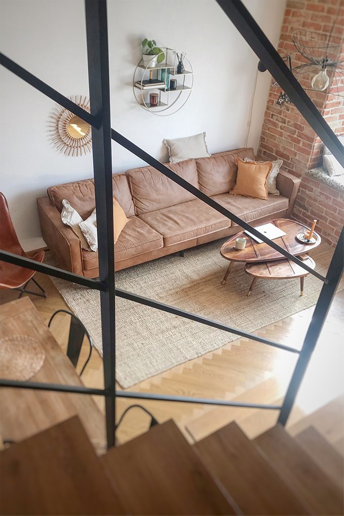 mieszkanie w stylu loft, cegła w mieszkaniu, styl vintage, industrialne elementy dekoracyjne, metalowa półka na ścianę, retro sofa, komplet stolików kawowych, stoliki drewniane