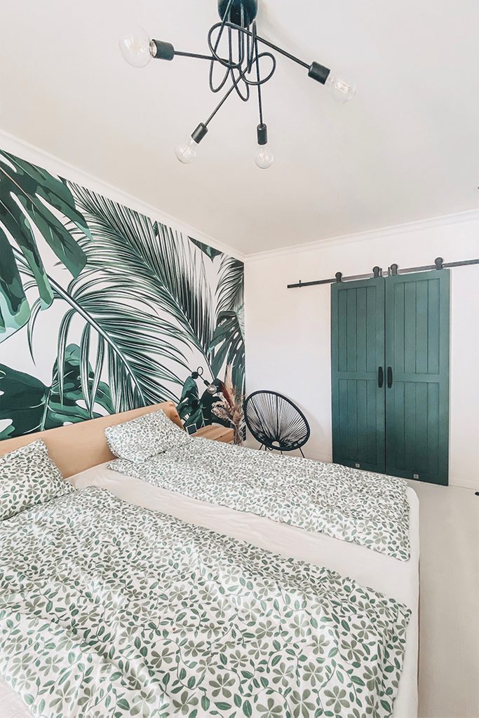 jasna sypialnia z dekoracyjną tapetą roślinną i garderobą ukrytą za zielonymi drzwiami przesuwnymi
