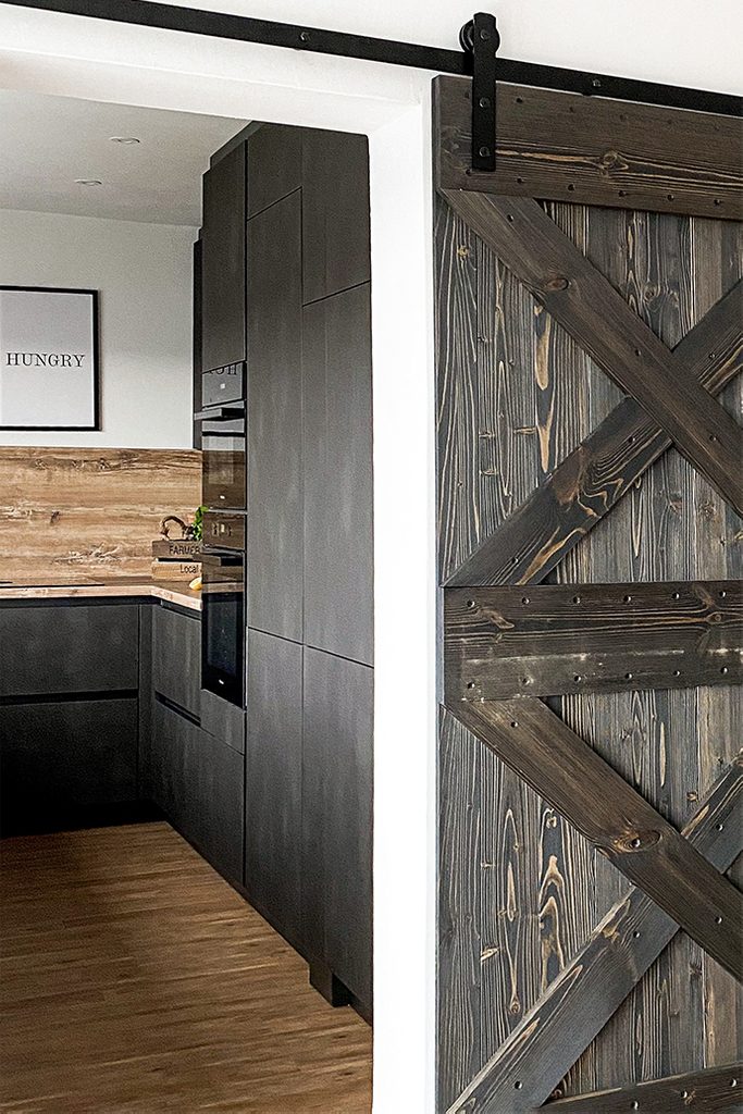 Wejście do kuchni z ciemną zabudową oddzielone drewnianymi drzwiami przesuwnymi w stylu rustykalnym