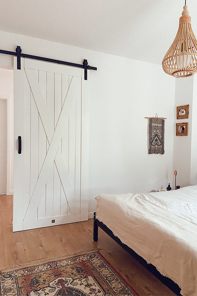 kolorowy dywanik i białe drzwi przesuwne obok dużego łóżka w sypialni