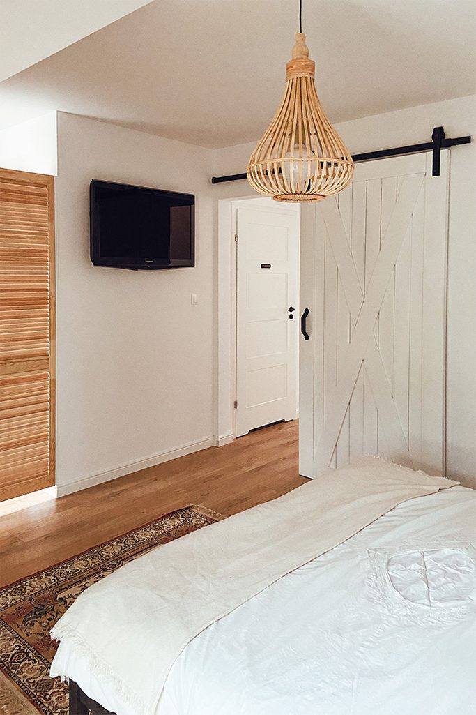 bambusowy żyrandol i białe drzwi przesuwne w sypialni z małą garderobą