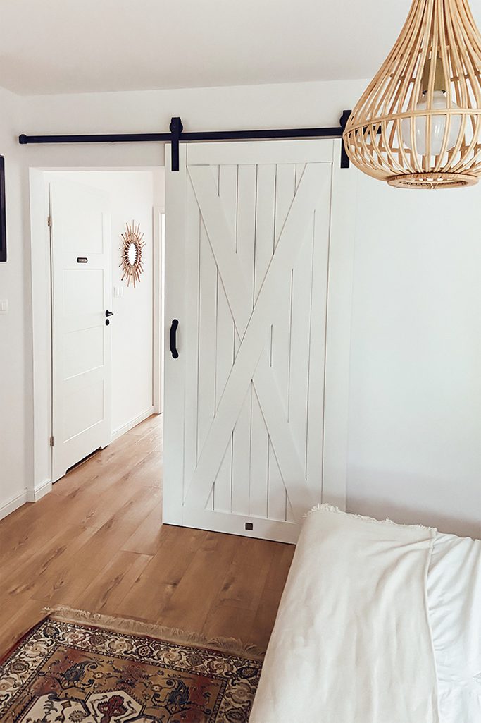 białe drzwi przesuwne obok dużego łóżka w sypialni