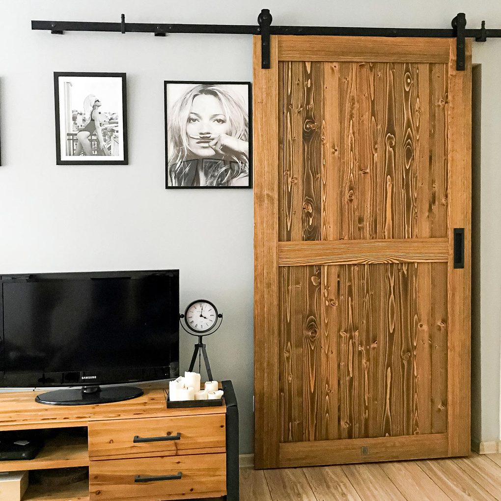 Drewniane drzwi na czarnym systemie przesuwnym zamontowane na ścianie udekorowanej czarno-białymi plakatami