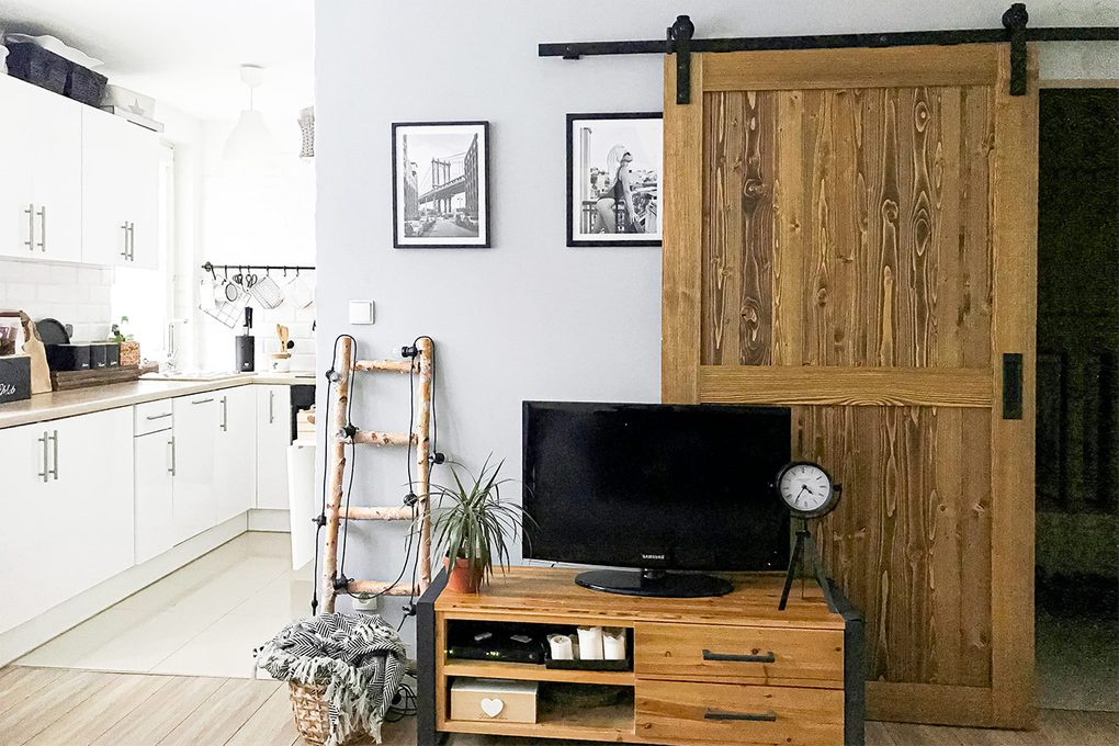 Drzwi przesuwne w małym mieszkaniu udekorowanym w bieli, drewnie i czarnych dodatkach