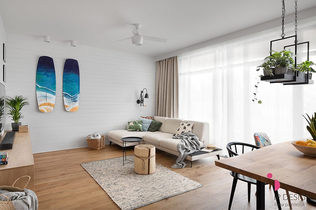 Jasny, przestronny salon z drewnianą podłogą, dużą jasną sofą i białymi ścianami