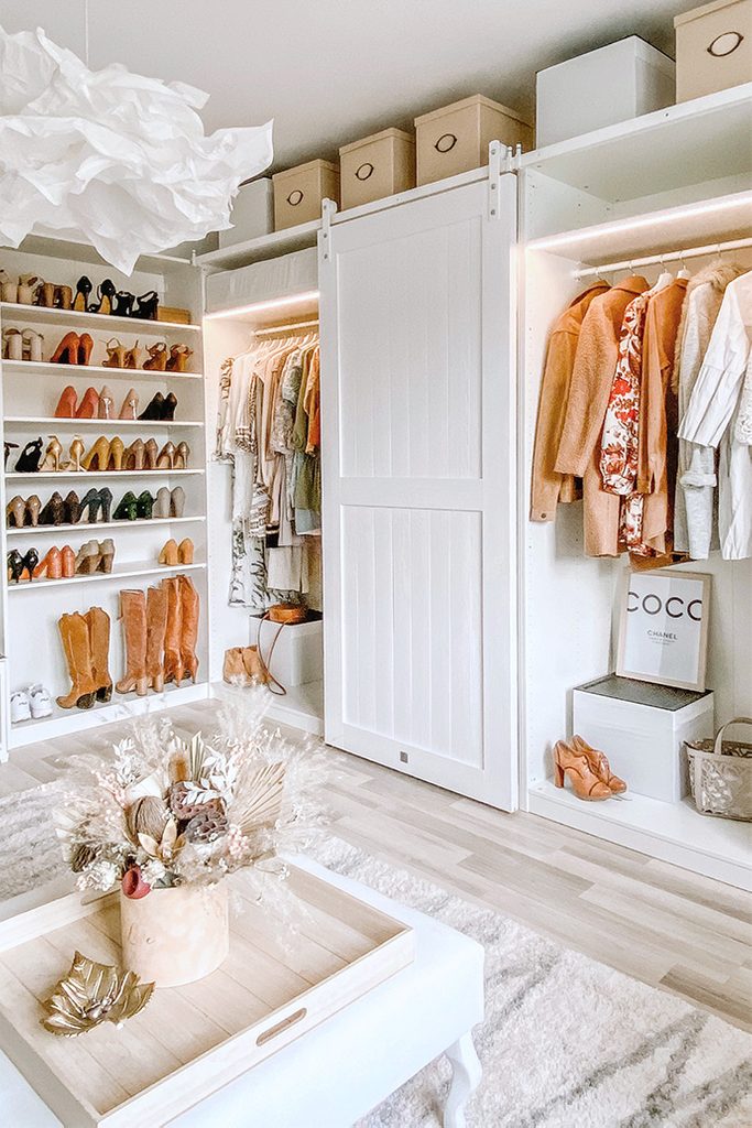 Białe szafy z ubraniami i białe półki z damskim obuwiem w dużej garderobie