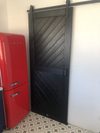 Czarne drzwi przesuwne koło czerwonej lodówki w kuchni