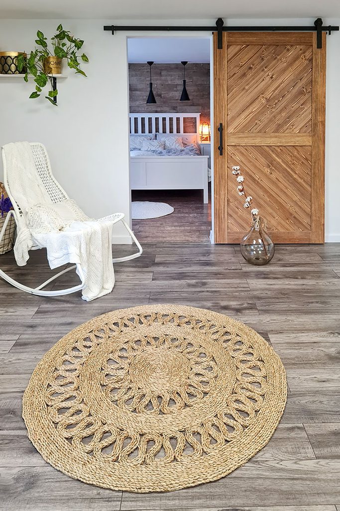 okrągły pleciony dywan z juty przed drzwiami przesuwnymi prowadzącymi do sypialni z białym łóżkiem