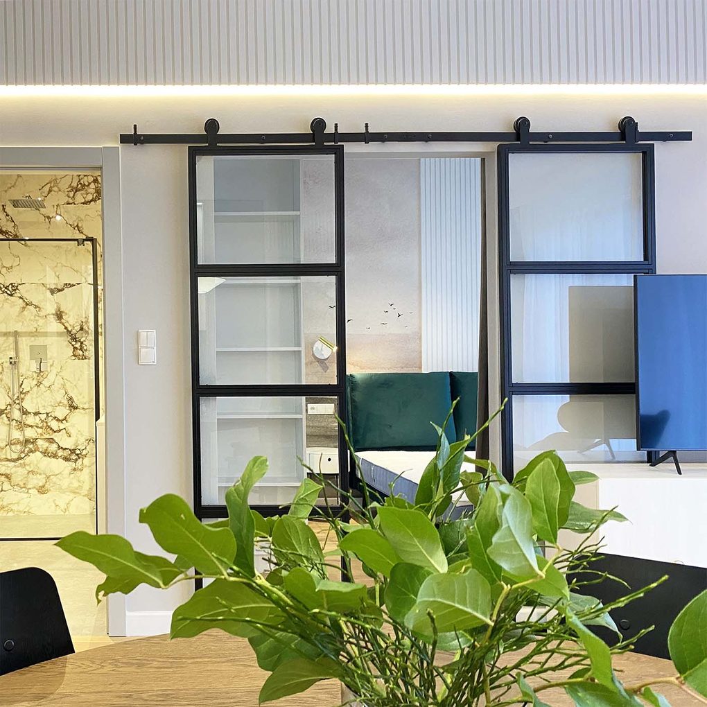 podwójne, szklane drzwi przesuwne oddzielające salon od sypialni w nowoczesnym mieszkaniu