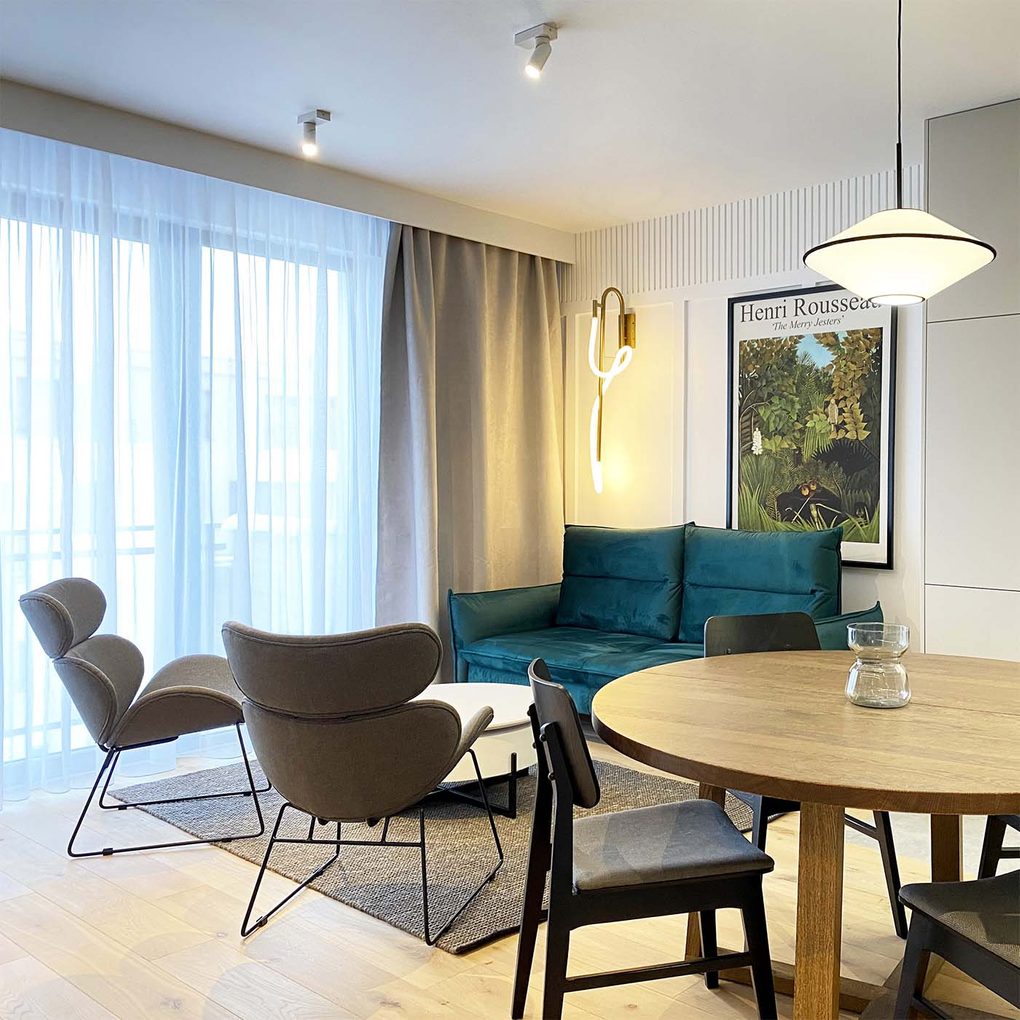 szmaragdowa sofa, szare fotele na czarnym stelażu oraz okragły stół w części jadalniano-salonowej nowoczesnego mieszkania