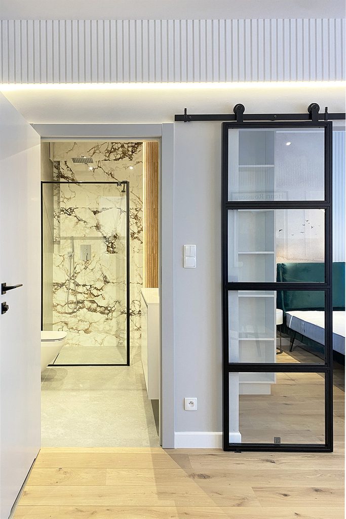 szklane drzwi przesuwne w czarnej ramie obok wejścia do nowoczesnej łazienki