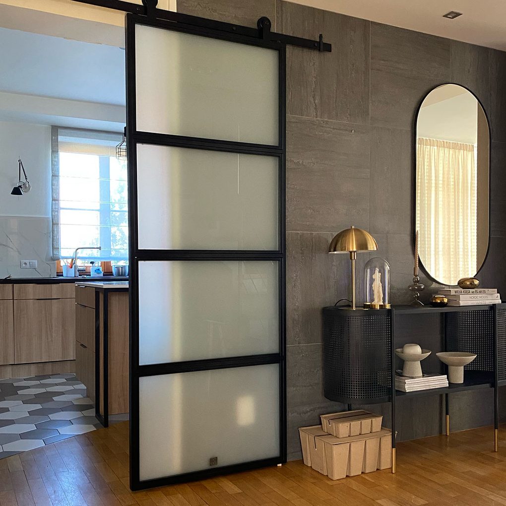 metalowe drzwi przesuwne przeszklone oddzielające kuchnię od przedpokoju oraz czarna konsola przy grafitowej ścianie z kafli