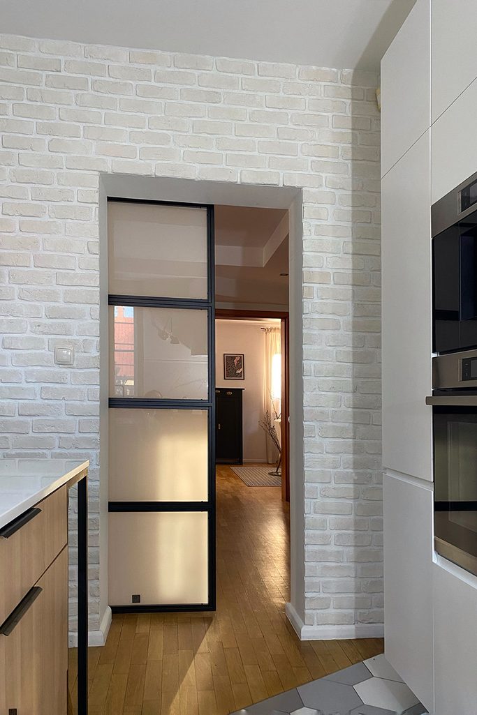 ściana z białej cegły w kuchni oraz drzwi przesuwne w metalowej ramie ze szkłem