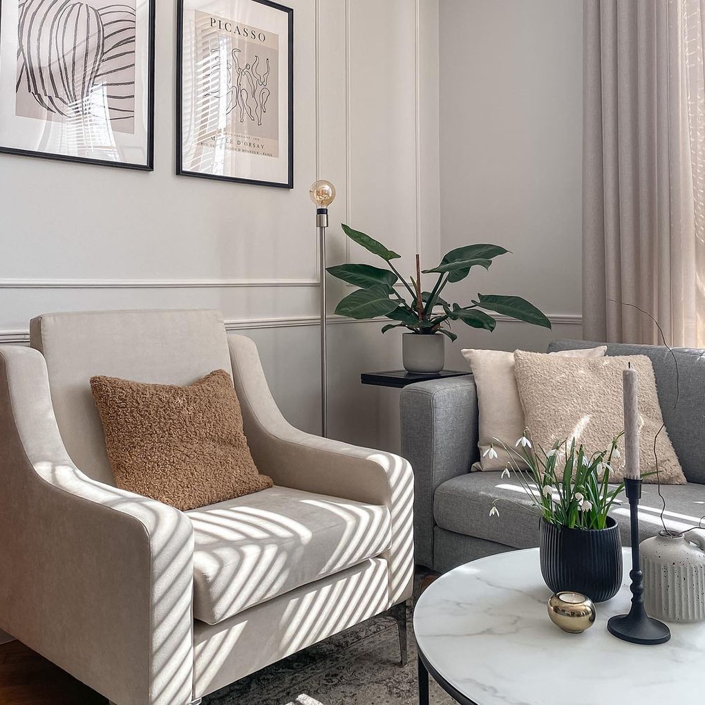 szara sofa i kremowy fotel na tle ściany zdobionej minimalistyczną sztukaterią w salonie