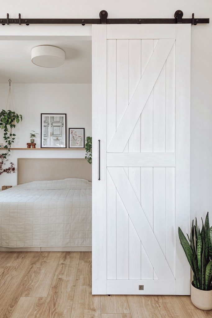 drewniane białe drzwi przesuwne w wejściu do sypialni z dużym łóżkiem