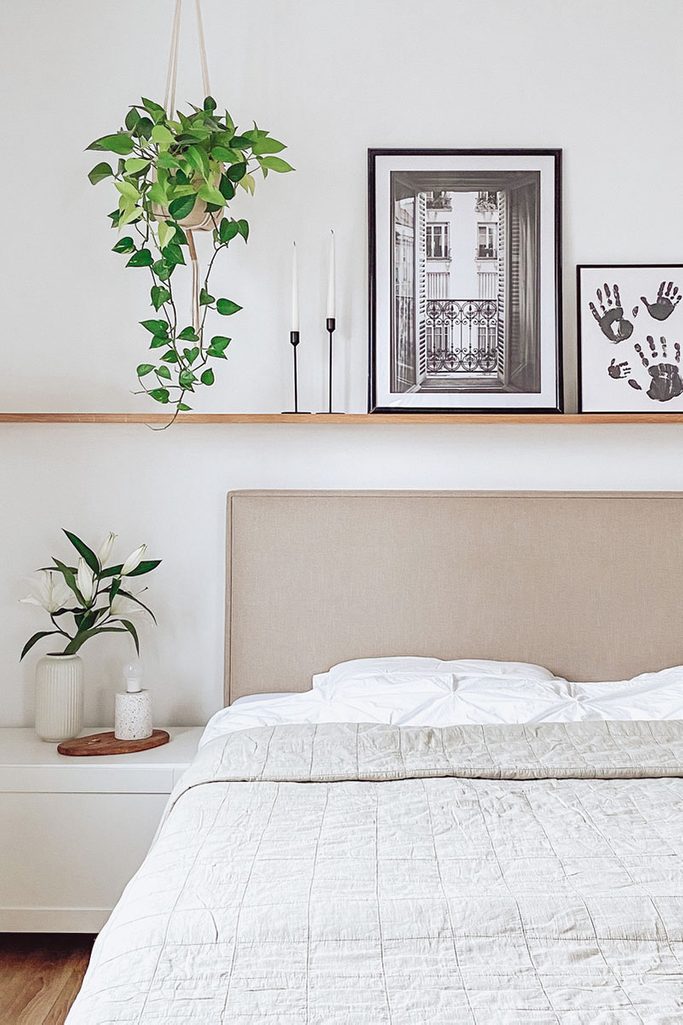 obrazki w czarnych ramkach nad łóżkiem z tapicerowanym zagłówkiem w białej sypialni