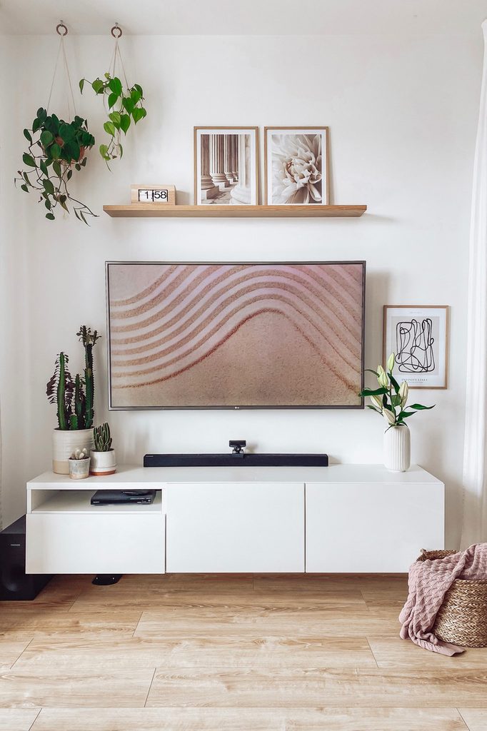 kącik TV z białą szafką oraz galerią obrazków w ramkach