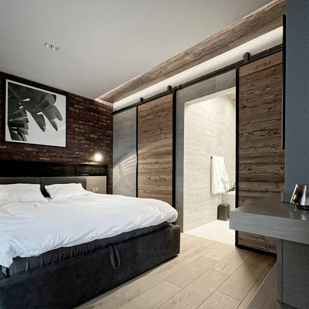 industrialne drzwi przesuwne do łazienki w sypialni urządzonej w stylu loftowym z czerwoną cegłą