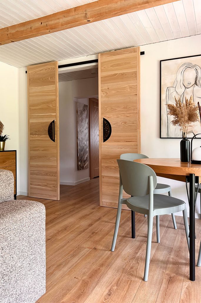 Drewniane designerskie drzwi przesuwne z czarnymi uchwytami w aranżacji pokoju gościnnego