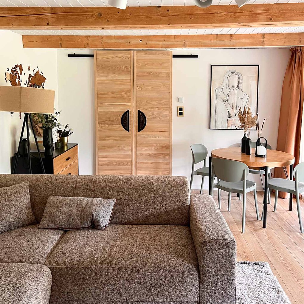 szaro-brązowa sofa oraz podwójne drewniane drzwi przesuwne w pokoju gościnnym urządzonym w barwach ziemi