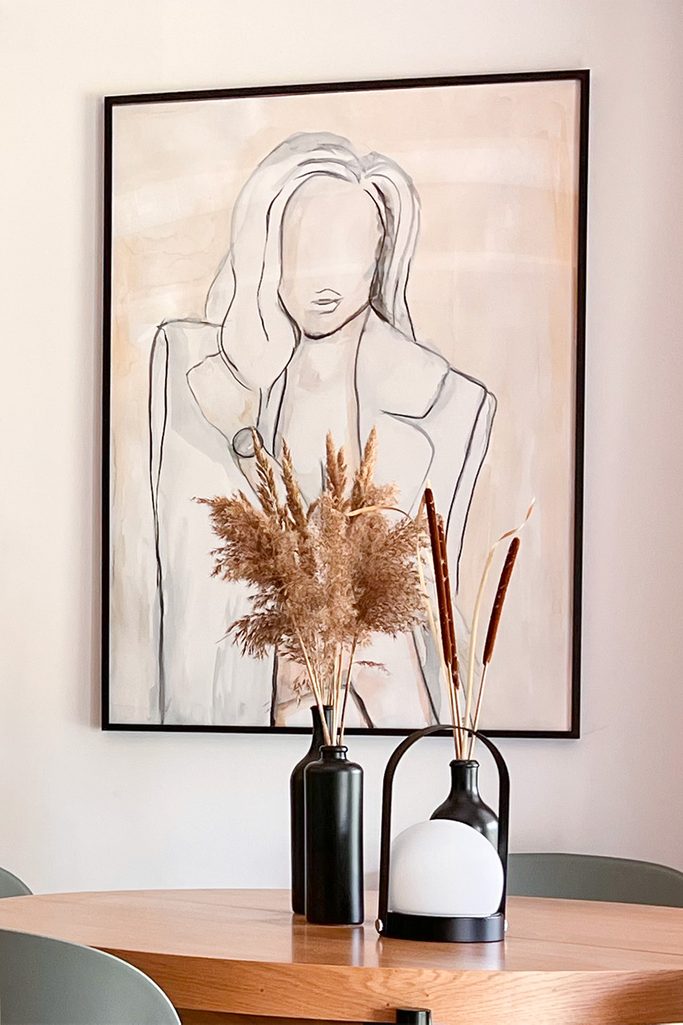 duży plakat w beżowo-brązowej tonacji w cienkiej czarnej ramie wiszący na ścianie nad okrągłym stołem