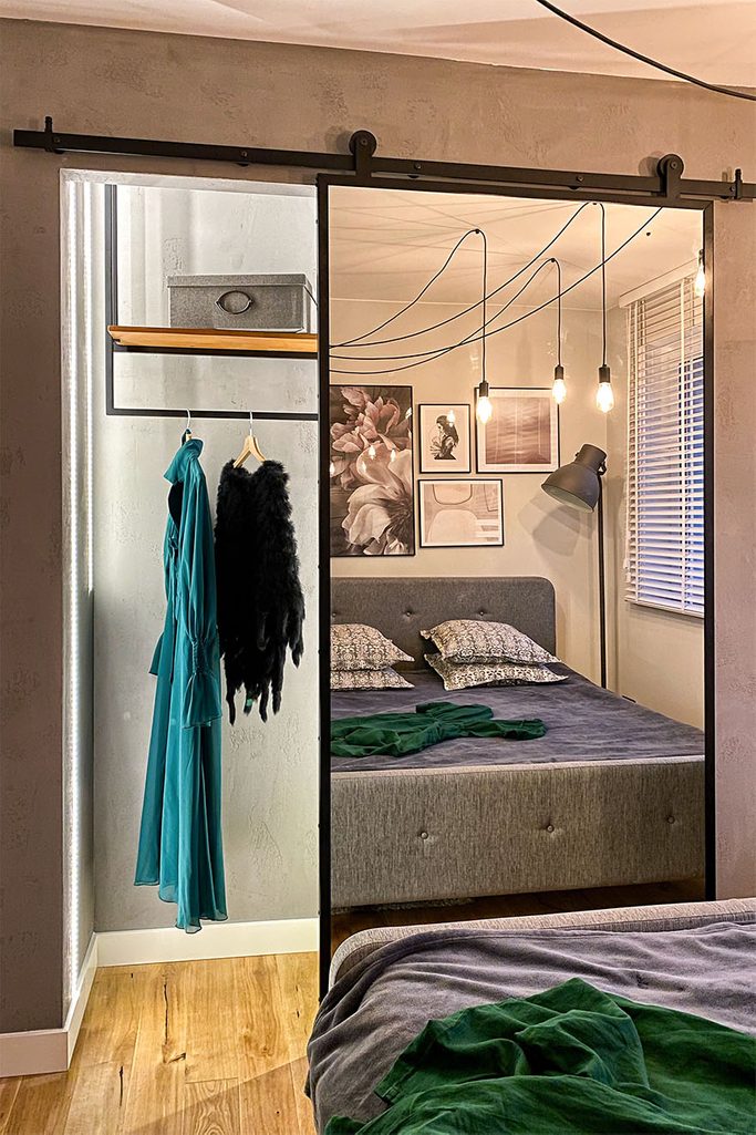 otwarte drzwi przesuwne ukazujące małą garderobę we wnęce w sypialni urządzonej w szarościach