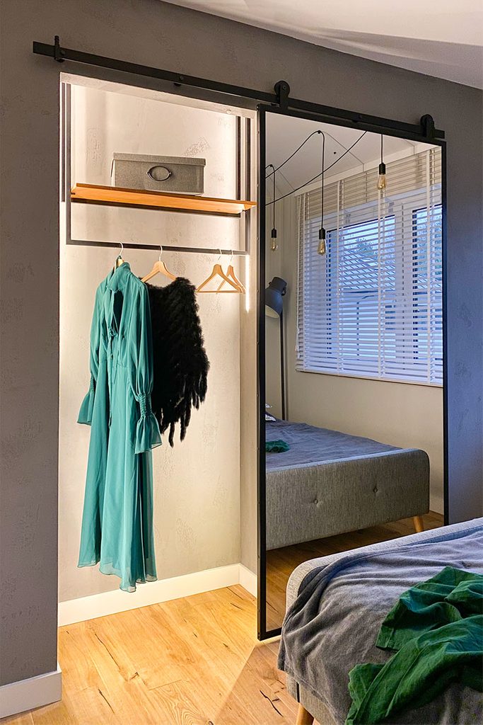 otwarte drzwi przesuwne ukazujące wnętrze małej garderoby w loftowej sypialni
