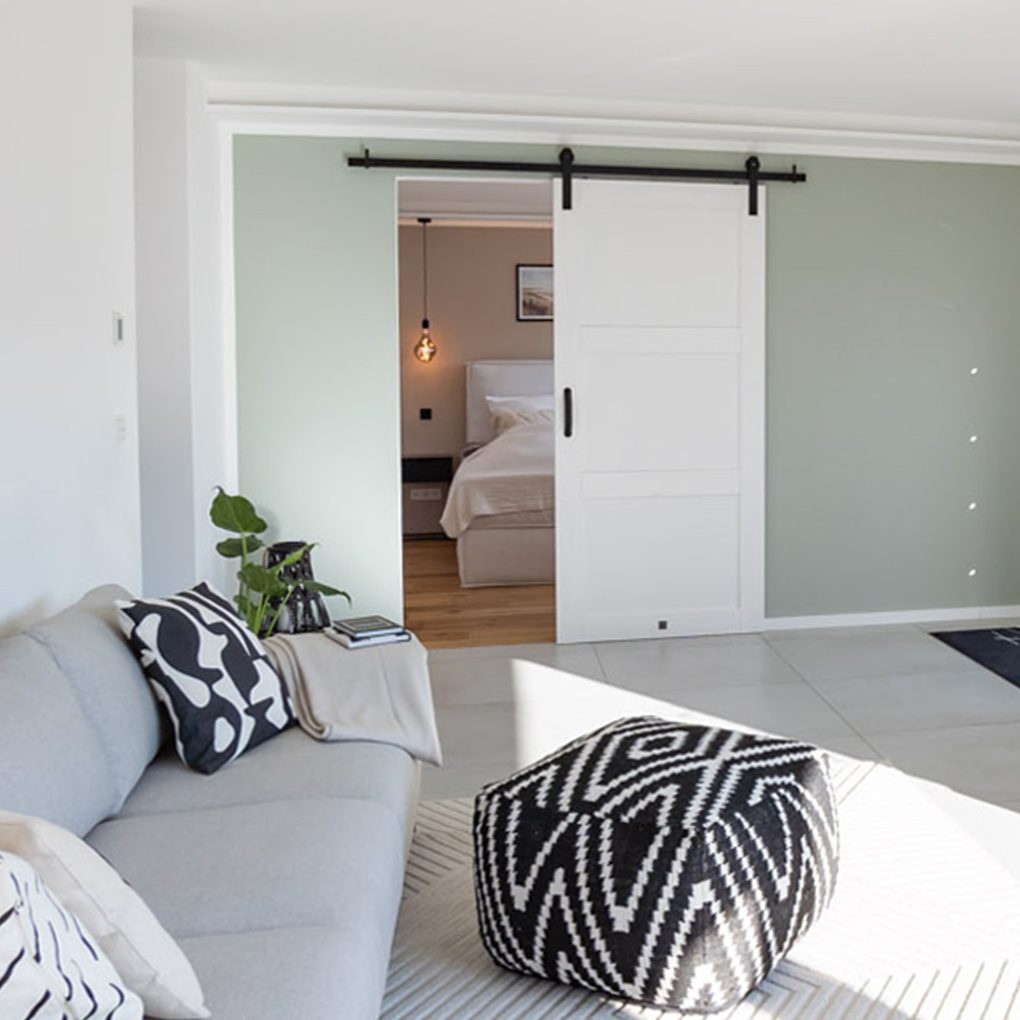 Szara sofa, białe drzwi przesuwne, minimalistyczne dekoracje w nowoczesnym salonie