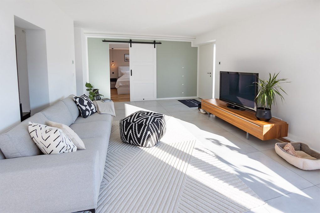 Szara sofa ozdobiona poduszkami w geometryczne wzory oraz szafka RTV w kąciku wypoczynkowym nowoczesnego salonu