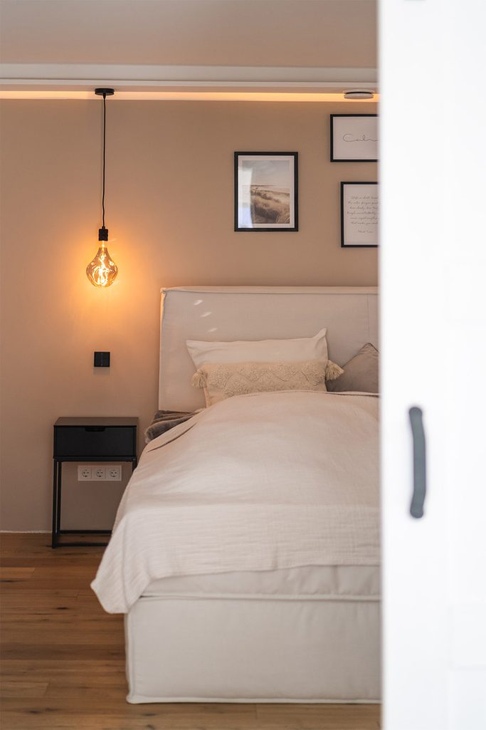 Lampa wisząca żarówka obok dużego łóżka w sypialni urządzonej w beżowych barwach