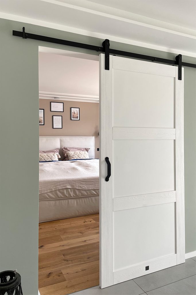Nowoczesne białe drzwi przesuwne, lekko otwarte, ukazujące sypialnię w beżowych kolorach