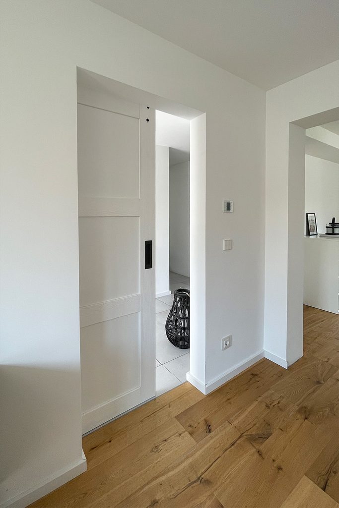 Białe drzwi przesuwne w sypialni z białymi ścianami bez dekoracji