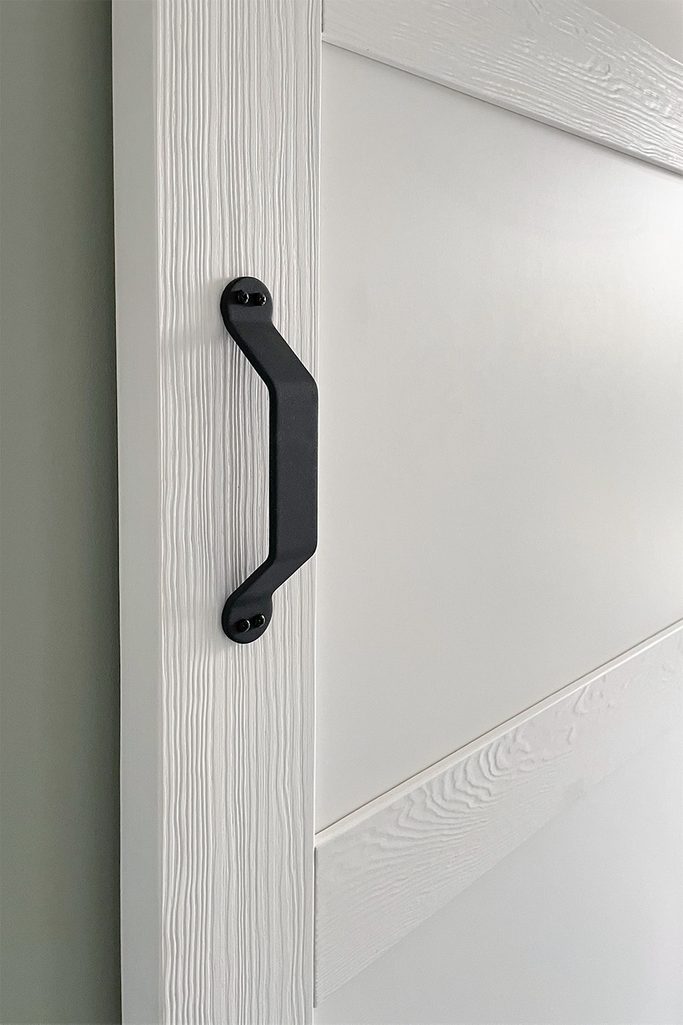 Czarna klamka do białych drzwi wykonanych z litego drewna