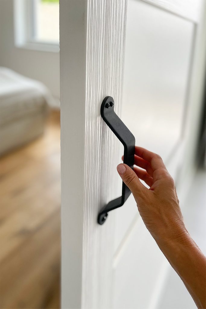 Czarna klamka na białych drzwiach z drewna głęboko szczotkowanego