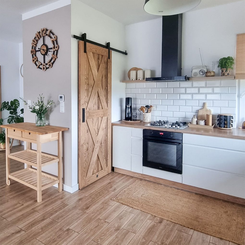 drewniane drzwi przesuwne zamykające spiżarnię w kuchni urządzonej w skandynawskim stylu z białymi szafkami i drewnianymi dodatakmi