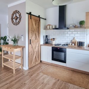drewniane drzwi przesuwne zamykające spiżarnię w kuchni urządzonej w skandynawskim stylu z białymi szafkami i drewnianymi dodatakmi