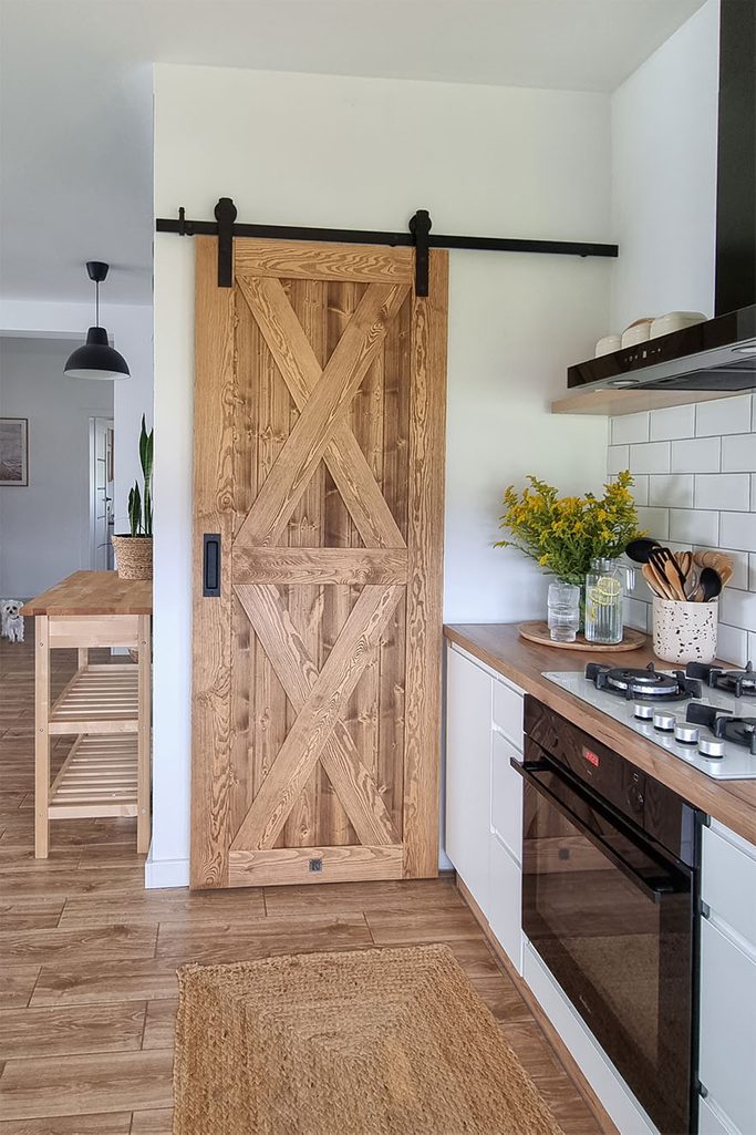 drewniane drzwi przesuwne zamykające spiżarnię przy jasnej kuchni z białymi szafkami w stylu skandyanawskim