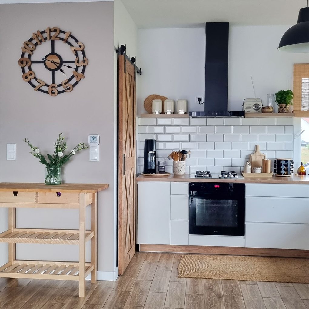 białe szafki kuchenne z drewnianym blatem przy drewnianych drzwiach do spiżarni