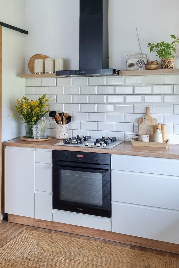 białe szafki kuchenne z drewnianymi blatami oraz białe płytki w skandynawskiej kuchni