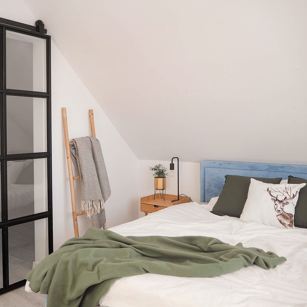 łóżko pod skosem na poddaszu w sypialni z małą garderobą