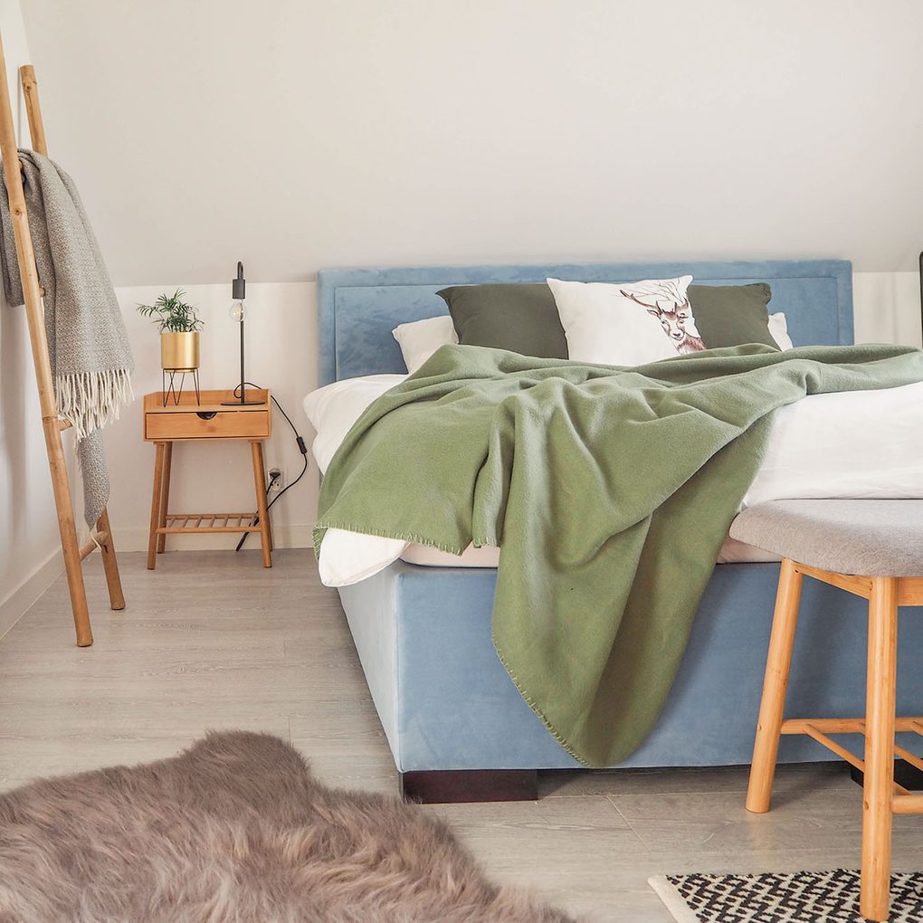 niebieskie tapicerowane łóżko oraz drewniane akcesoria w małej sypialni na poddaszu
