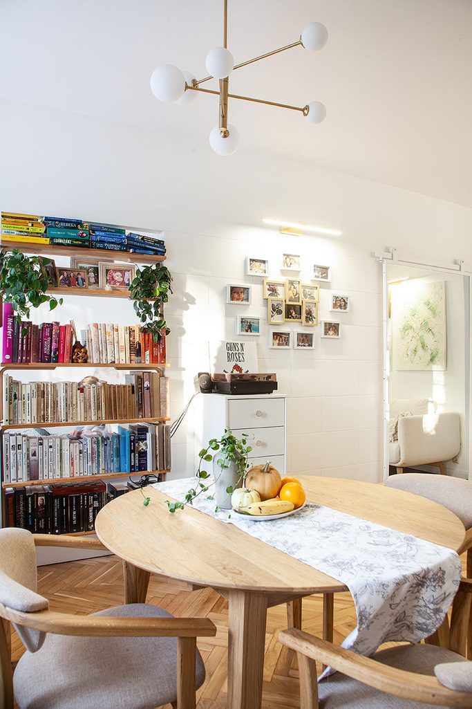 okrągły drewniany stół i regał z ksiązkami we wnętrzu małego mieszkania