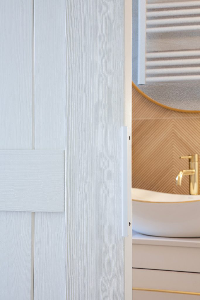uchylone białe drewniane drzwi ukazujące fragment łazienki