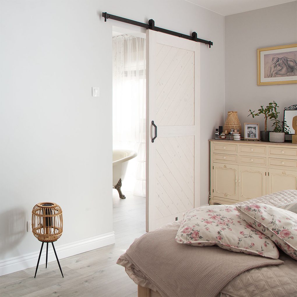 sypialnia z łazienką rozdzielone białymi drewnianymi drzwiami przesuwnymi w stylu rustykalnym