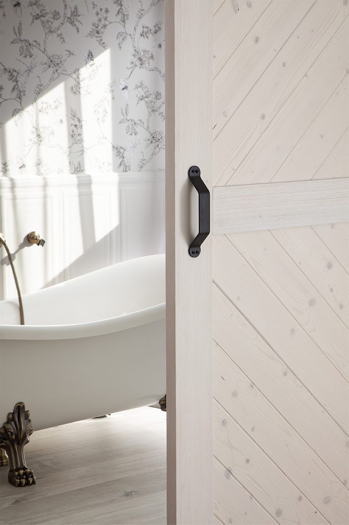 otwarte białe drzwi drewniane ukazujące fragment łazienki z wolnostojącą wanną