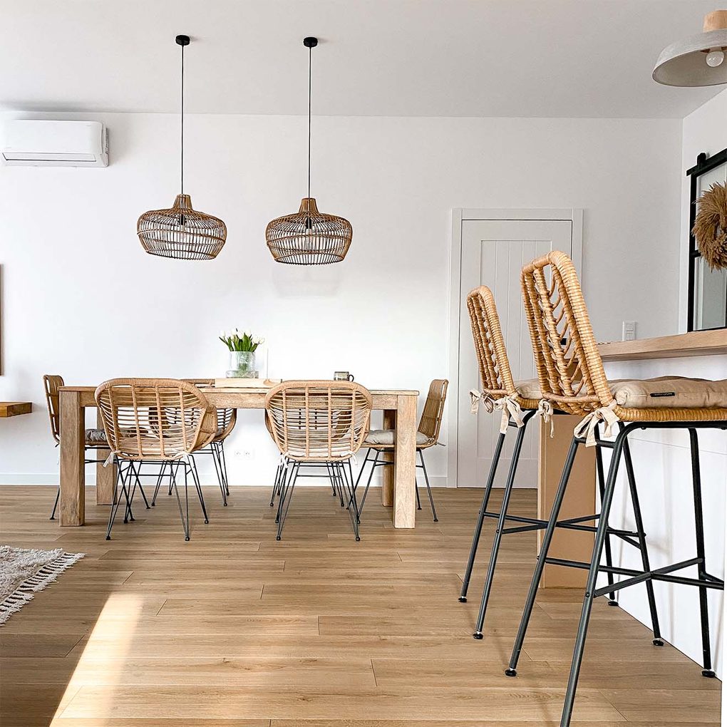 rattanowe krzesła na metalowych nogach, rattanowe stołki barowe oraz wiklinowe lampy wiszące w salonie z białymi ścianami