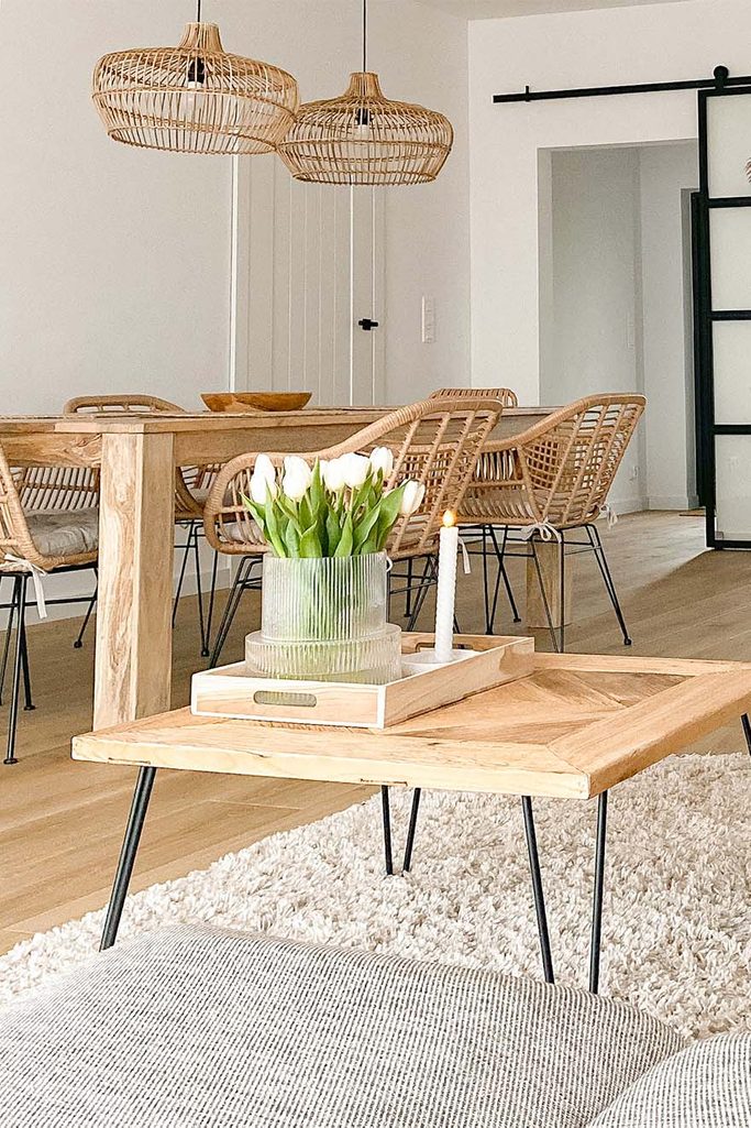 kwadratowy stolik kawowy na metalowych nogach oraz duży drewniany stół z rattanowymi krzesłami w salonie z białymi ścianami